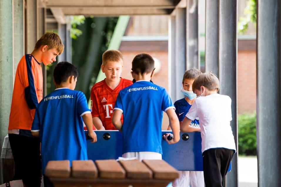 Sechs Kinder spielen gemeinsam mit einem Tischkicker unter einem überdachten Bereich.